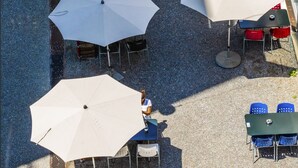 An outdoor seating area with multiple tables and umbrellas, a sign for 'Ziv Back Hotel Take Away', and a chalkboard menu.