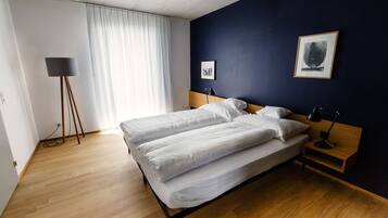 Ein Doppelbett mit weißer Bettwäsche, ein Nachttisch mit Lampe, eine Stehlampe und ein gerahmtes Bild an der Wand.