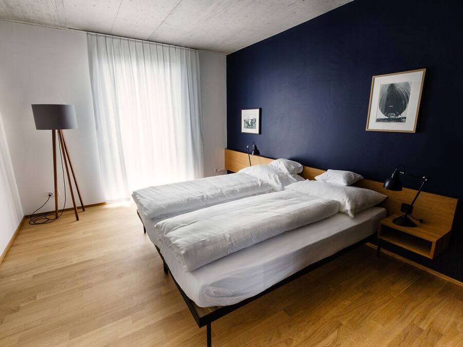 Ein Doppelbett mit weißer Bettwäsche, ein Nachttisch mit Lampe, eine Stehlampe und ein gerahmtes Bild an der Wand.