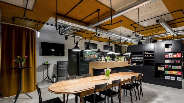 A modern dining area with a wooden table and black chairs, a bar area with a counter and shelves, and a large black refrigerator.
