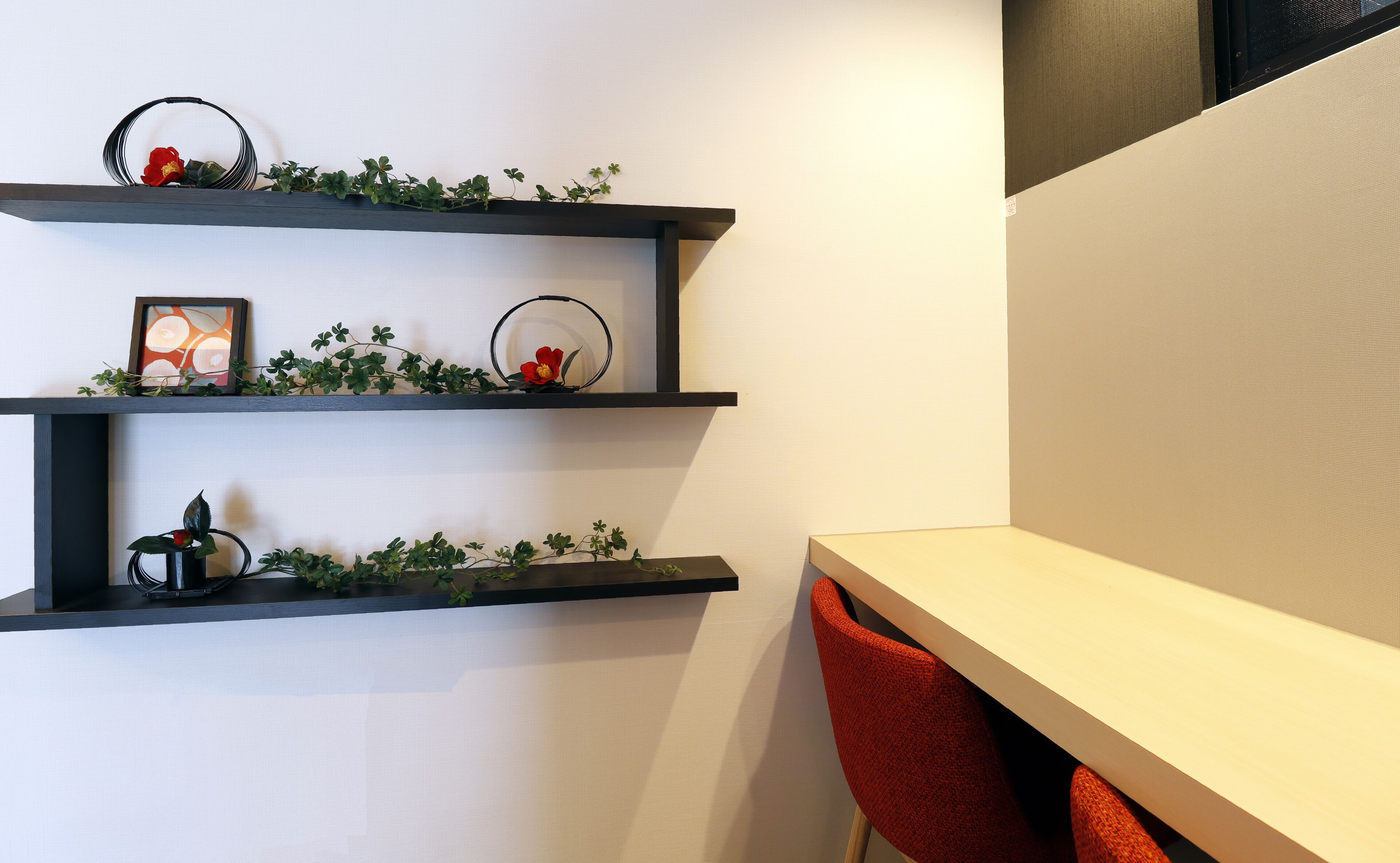 A modern interior with three black shelves against a white wall, each adorned with greenery and small decorative items.