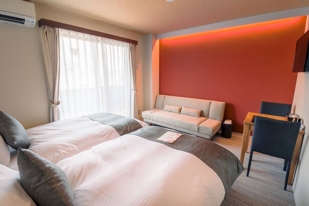 A hotel room with two beds, a sofa, a desk, and a chair.
