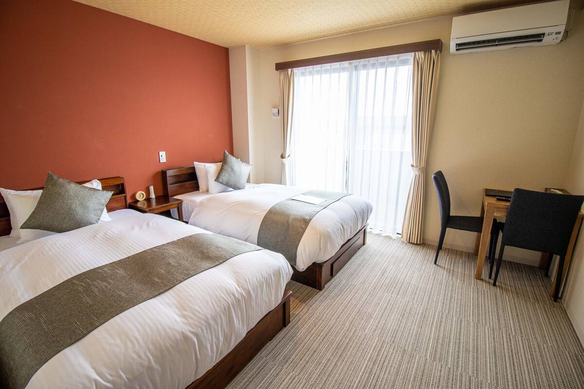 A hotel room with two beds, a desk, a chair, and an air conditioning unit.