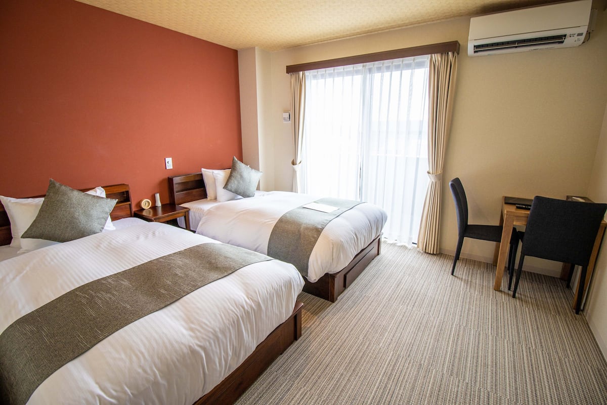 A hotel room with two beds, a desk, a chair, and an air conditioning unit.