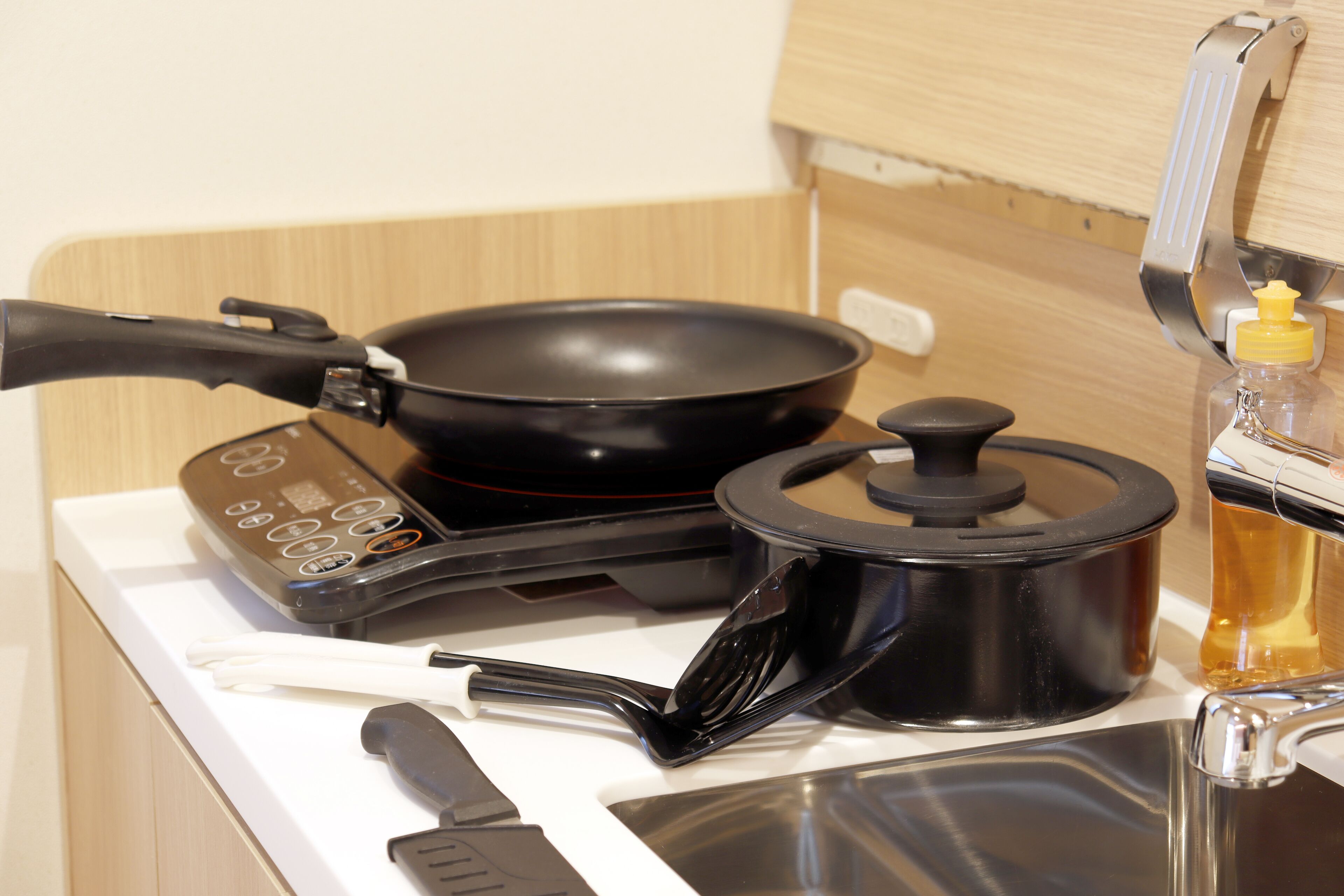 A kitchen with a stove, a frying pan, a pot, a bottle of oil, and a faucet.