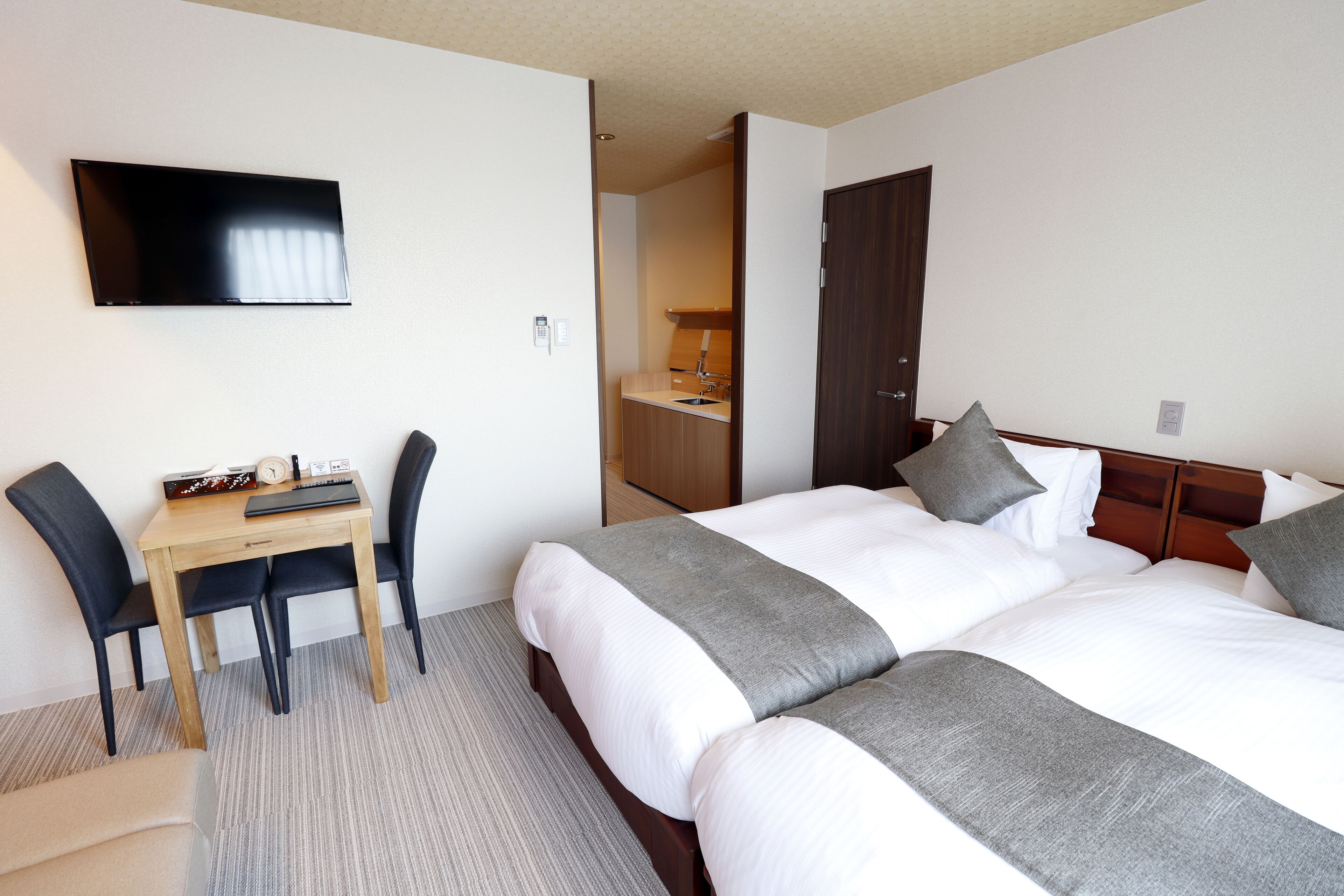 Hotellihuone, jossa on kaksi sänkyä, työpöytä tuoleineen, televisio ja pieni keittonurkkaus.