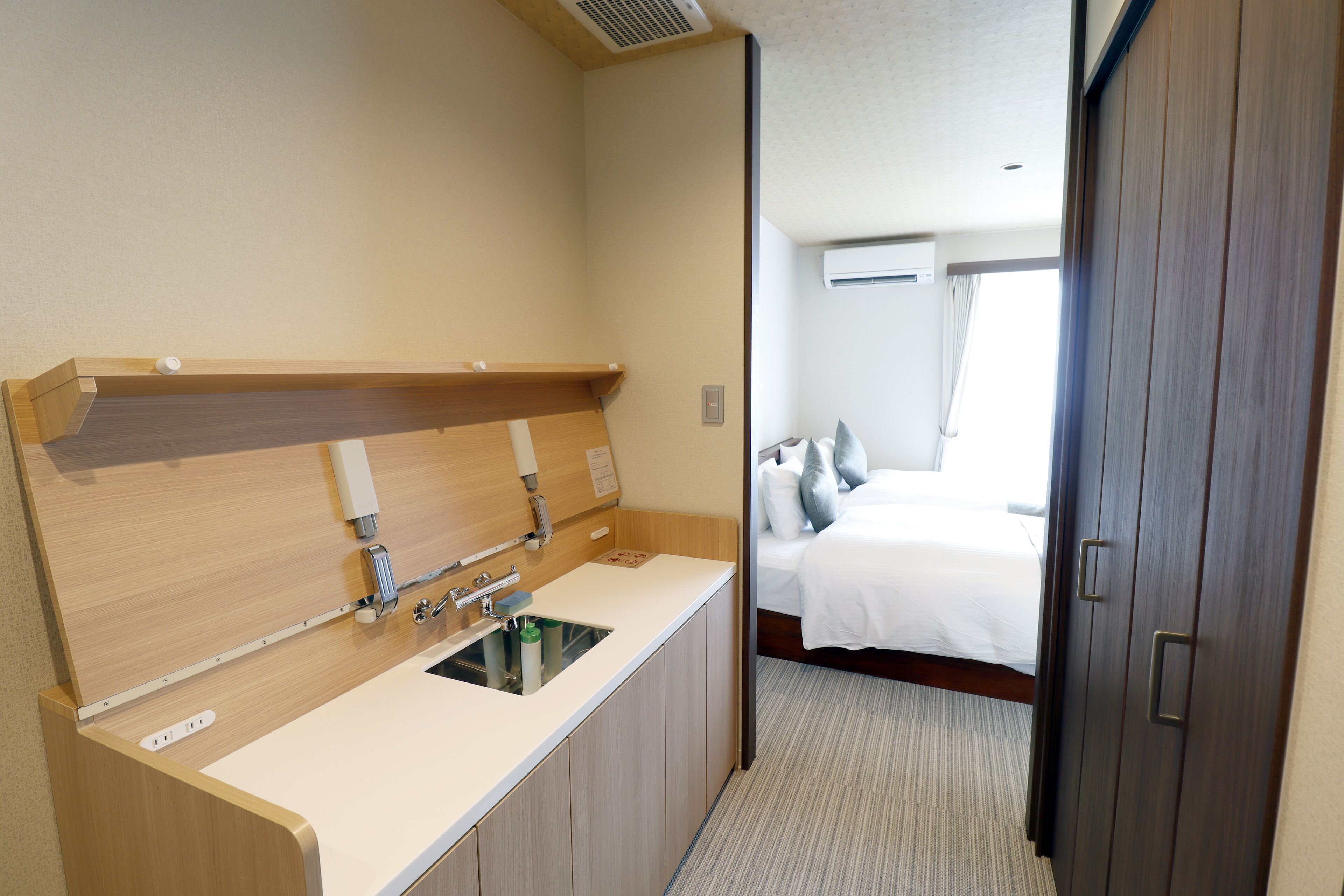 A hotel room with a wooden vanity, a sink, and a bed with white bedding.