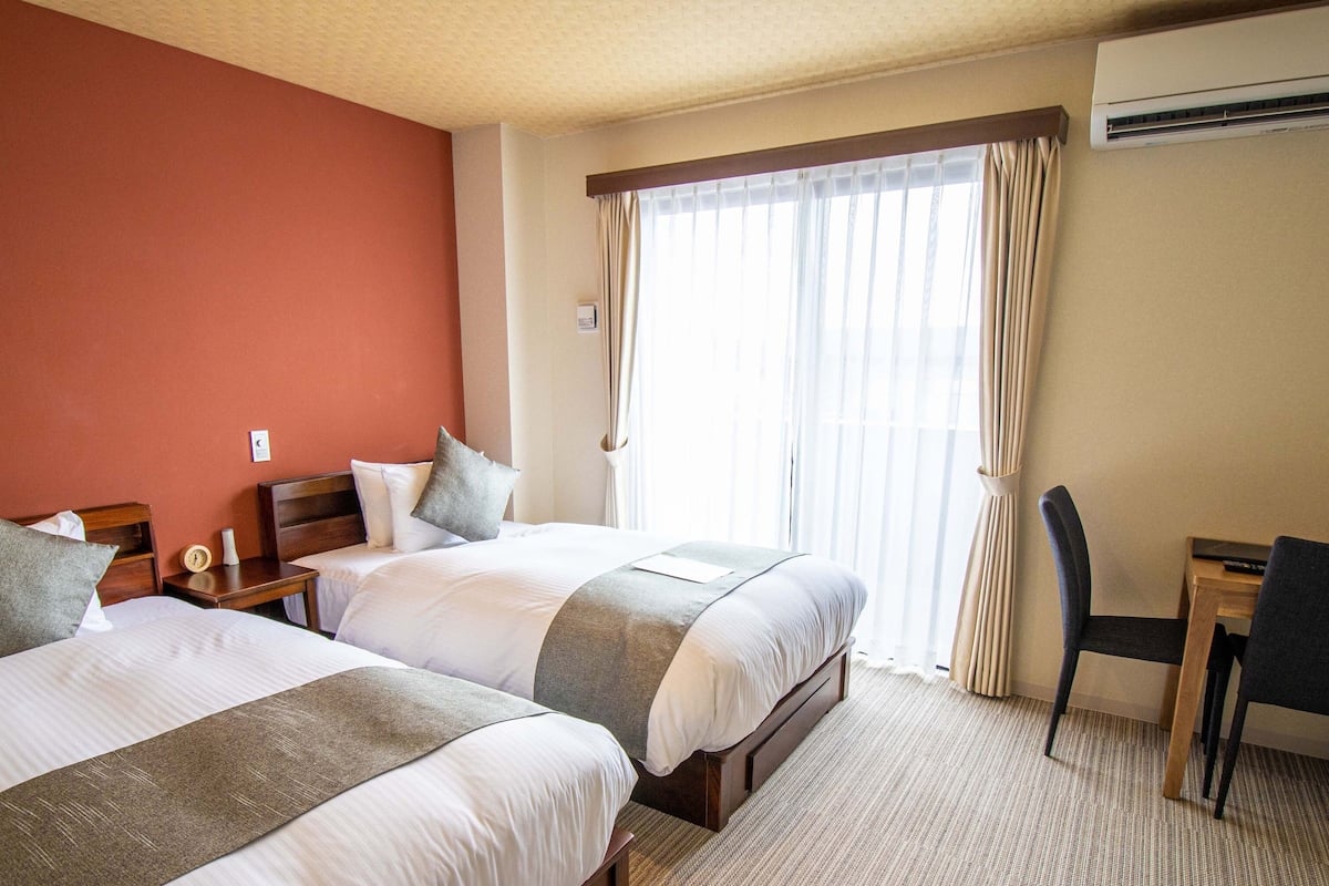 A hotel room with two beds, a desk, a chair, and a window with curtains.