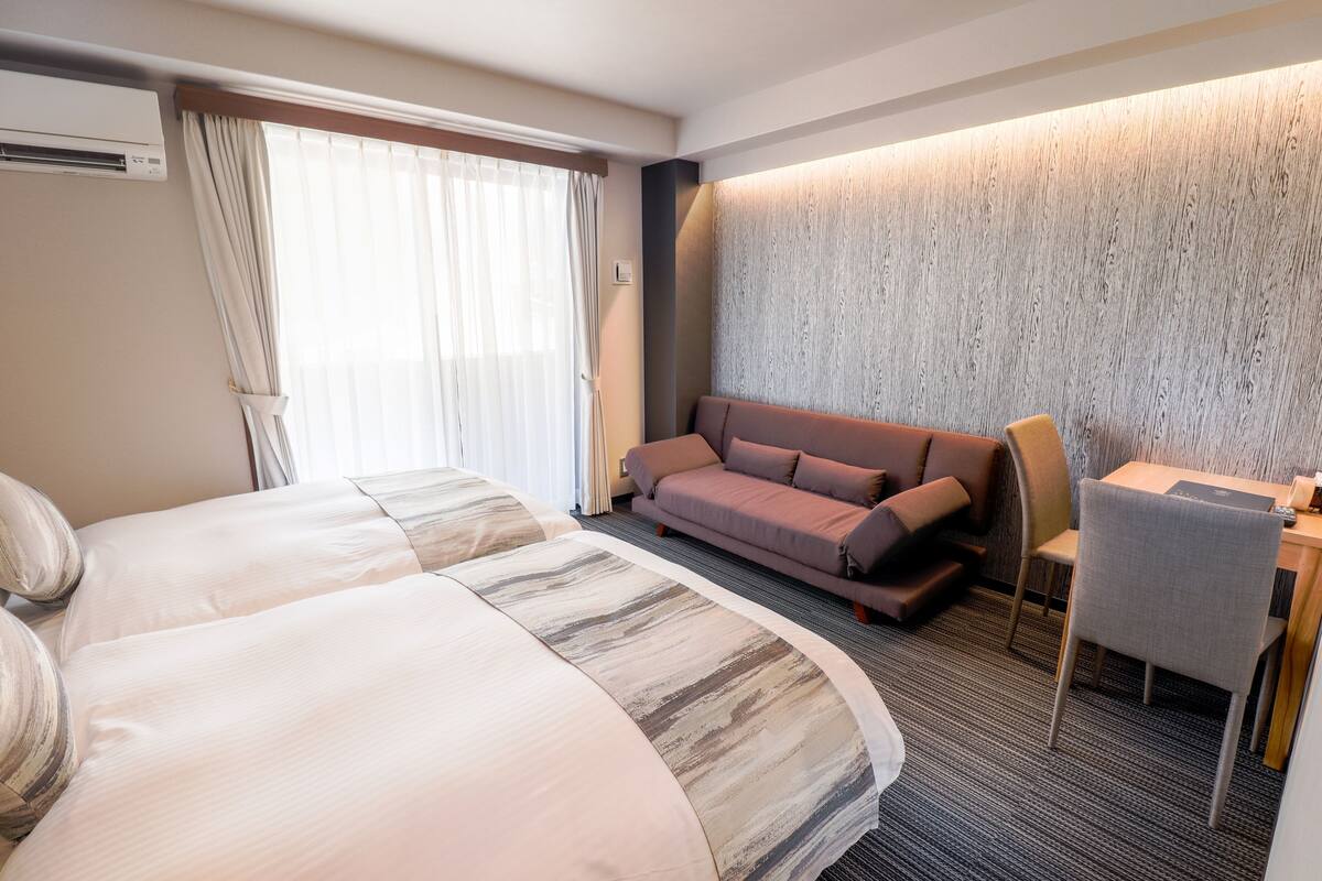 A hotel room with two beds, a sofa, a desk, and a chair.