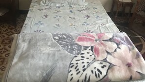 A bed with floral bedding, a headboard, a bedside table with a lamp, and a chair.