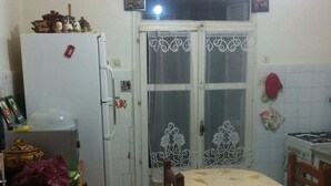 A compact kitchen with a refrigerator, a dining table, and a tiled floor.
