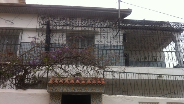 A building with a tiled entrance, a metal fence, and a tree with purple flowers.