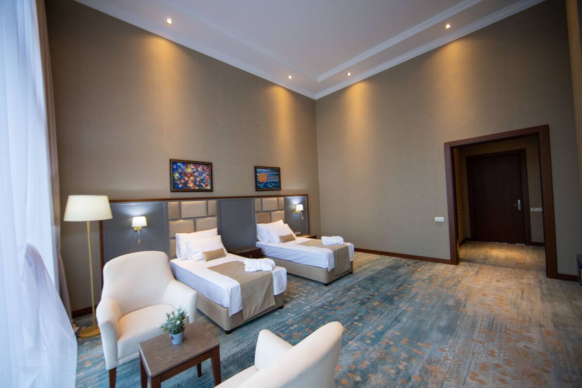 A hotel room with two beds, a chair, a small table, and a potted plant.