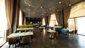 A spacious restaurant with high ceilings, modern lighting fixtures, and a variety of seating arrangements. - Saat Meydani Hotel (Nakhchivan)