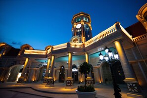 A grand hotel with a clock tower, large columns, and a well-lit entrance.