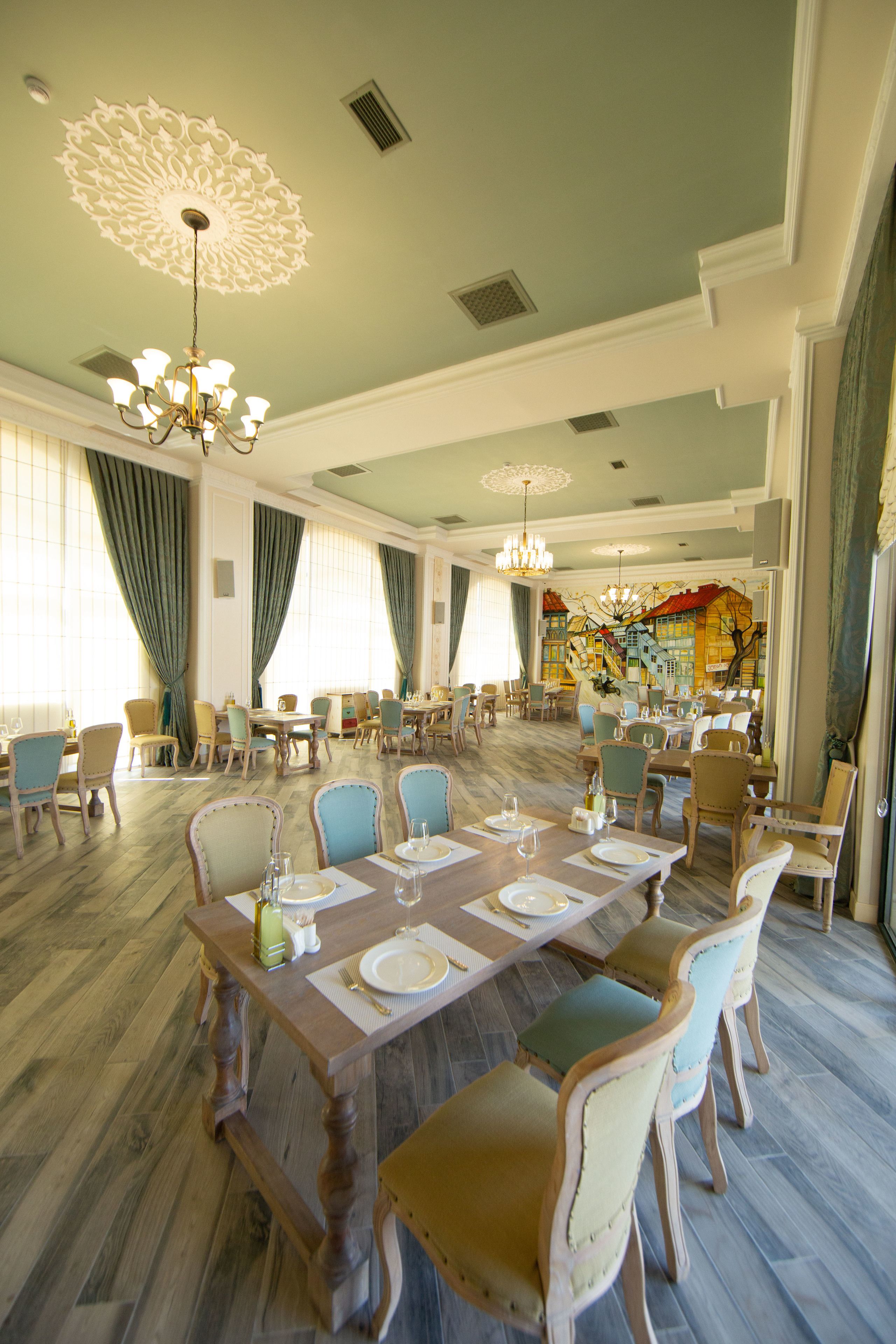 Un comedor espacioso con varias mesas y sillas, candelabros elegantes y un mural grande en la pared.