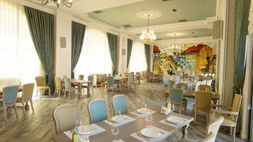 Un comedor espacioso con varias mesas y sillas, candelabros elegantes y un mural grande en la pared.