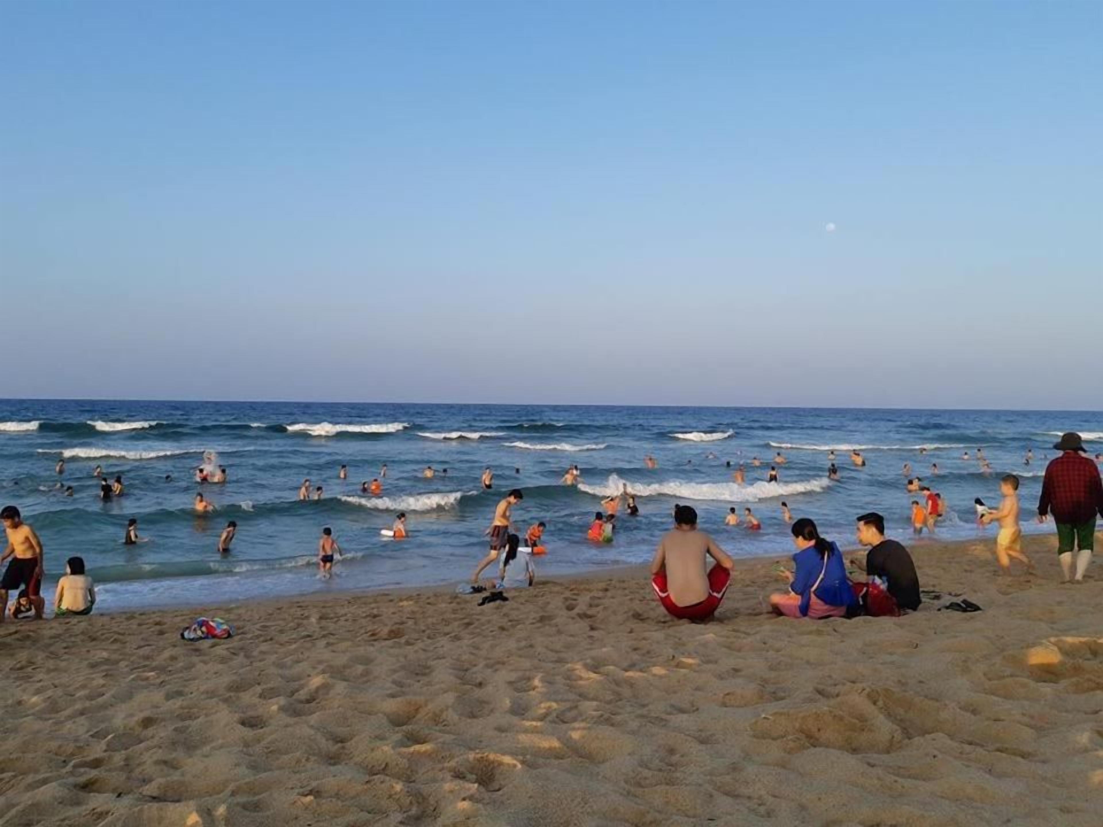 A beach with people swimming and walking on the sand.