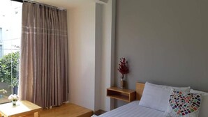 A bedroom with a bed, a nightstand, a wooden table, and a window with curtains.