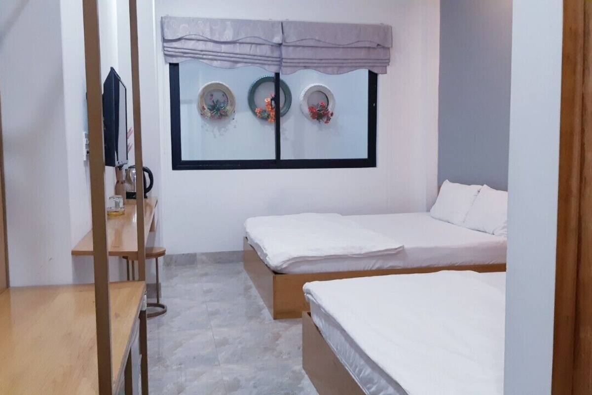 Une petite chambre propre, avec deux lits simples, un bureau en bois et une fenêtre décorée d’assiettes.