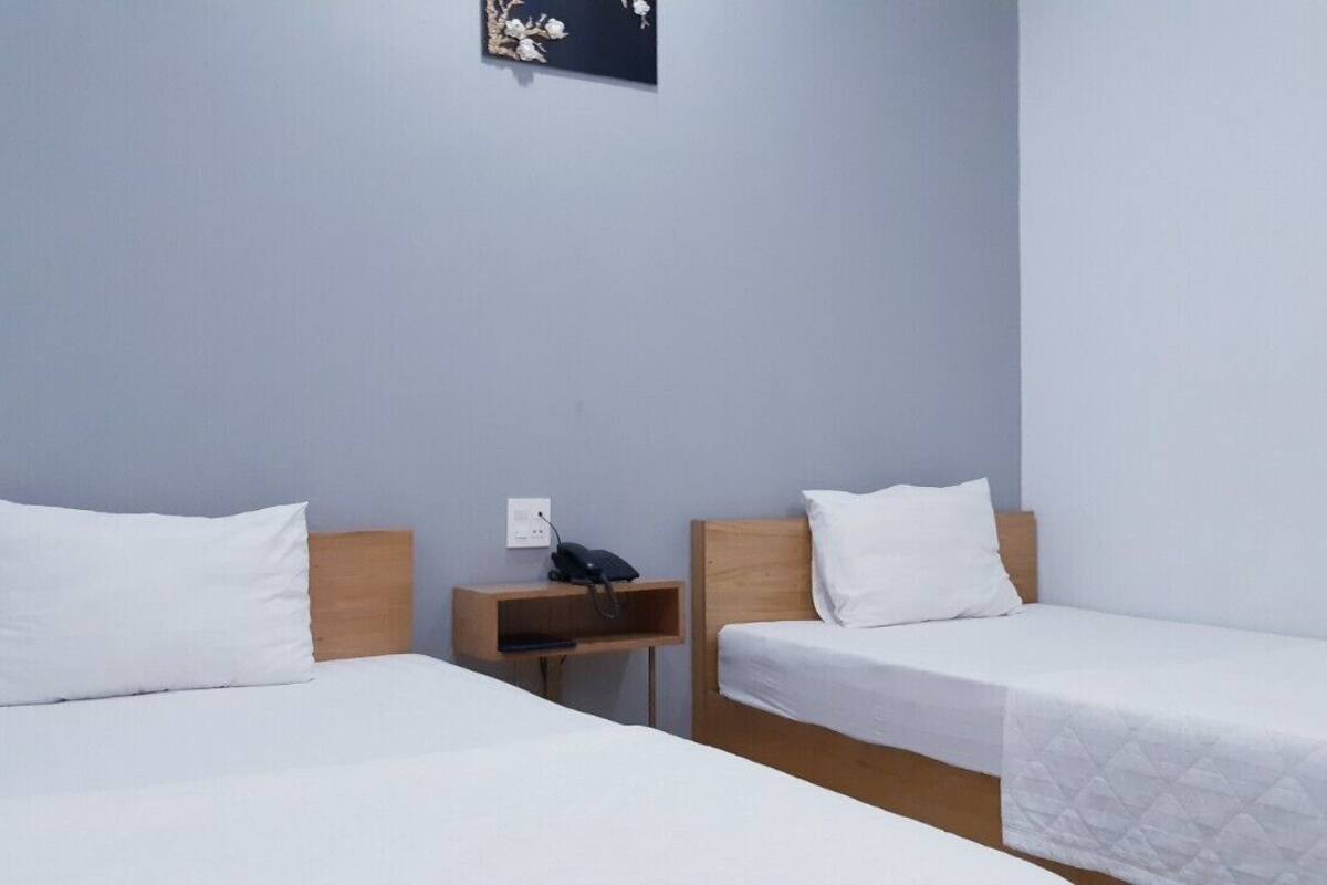 Une chambre d’hôtel avec deux lits simples, une table de chevet en bois avec un téléphone et un interrupteur fixé au mur.