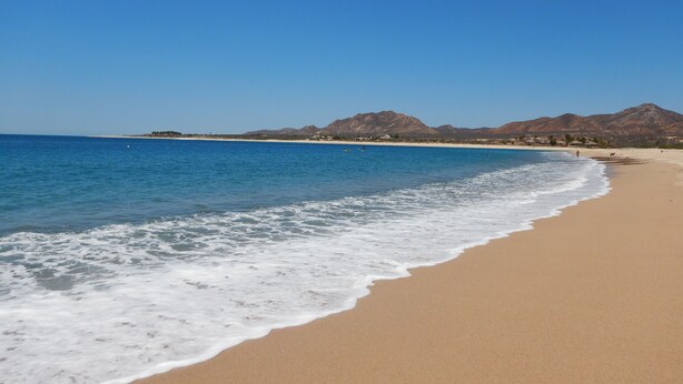 A beach with clear blue water, a sandy shore, and mountains in the background.