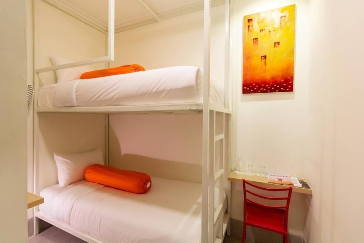 A bunk bed room with a desk and chair, a painting on the wall, and a window.