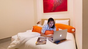 A person lying on a bed with an open laptop, a magazine, and orange pillows. - Front One Residence Syariah Mampang (Jakarta)