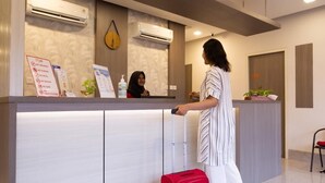 A reception desk with a sign listing room rules, a red suitcase, and a potted plant. - Front One Residence Syariah Mampang (Jakarta)