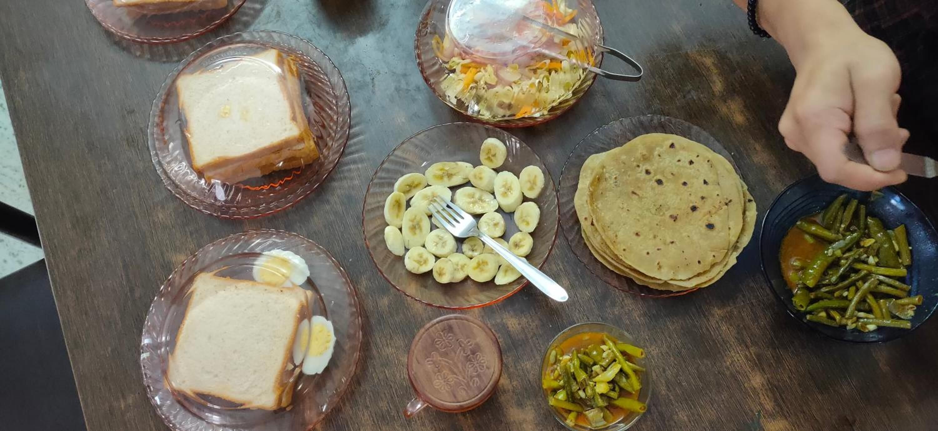 A table with various food items including bread, bananas, a stack of tortillas, and a bowl of green beans.