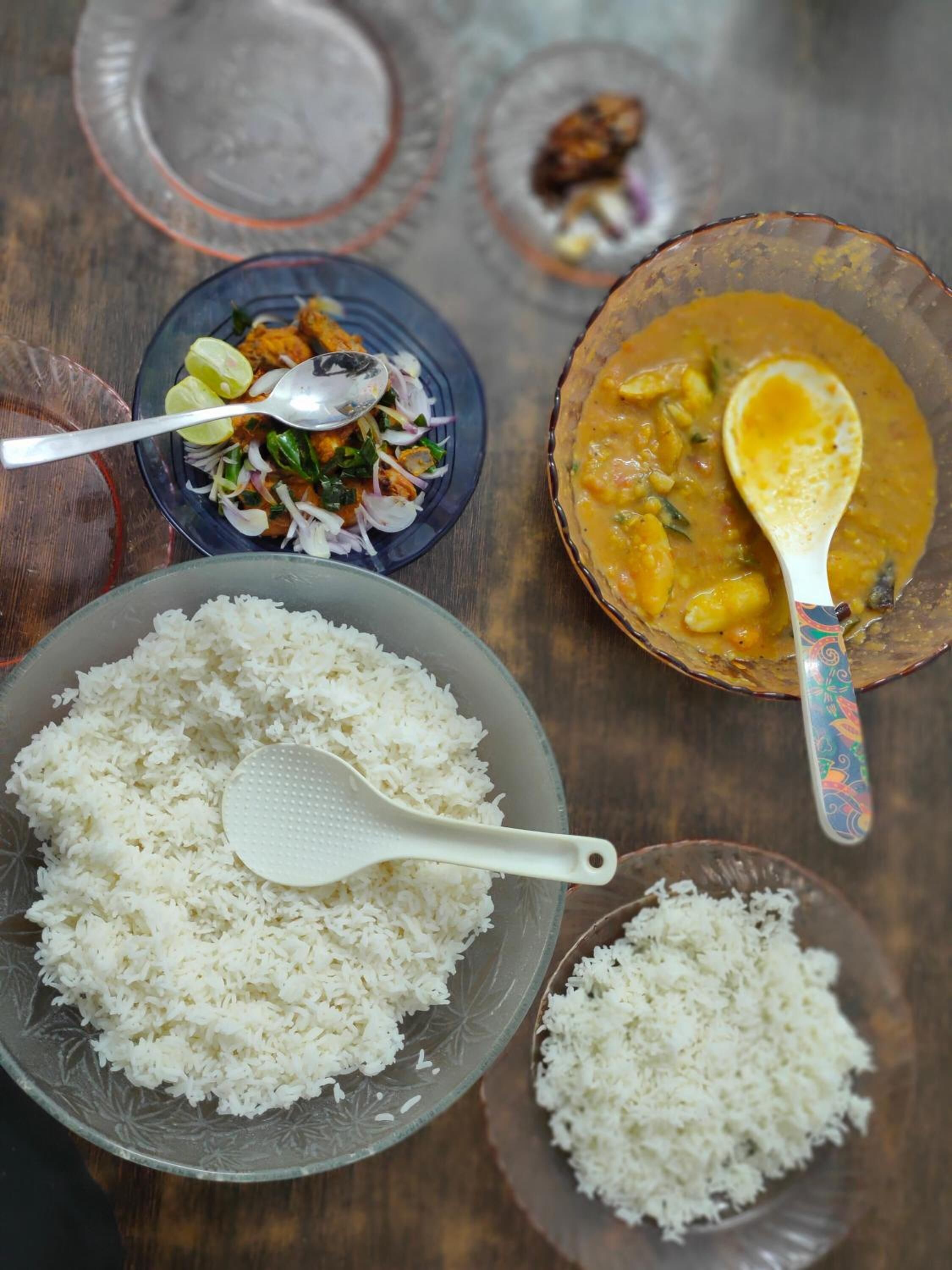 A table with white rice, a bowl of curry, and a salad with a spoon.