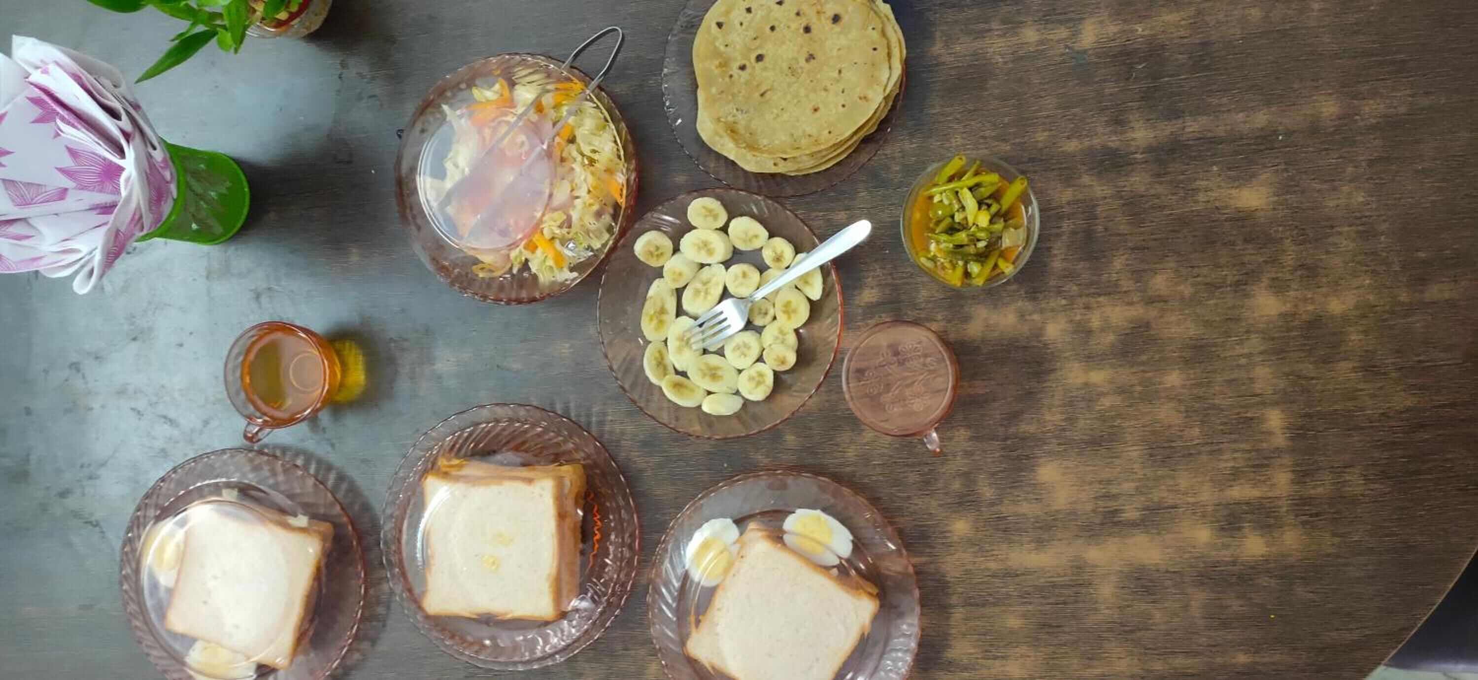 A table with various food items including sliced bananas, a bowl of salad, and a stack of tortillas.