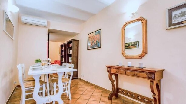 A dining area with a white table and chairs, a wooden console table with a mirror, and a bookshelf in the background. - Lovely Studio in Trastevere (Rome)