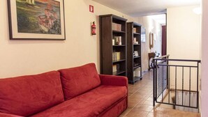 A red sofa in a hallway with a bookshelf and a fire extinguisher on the wall. - Lovely Studio in Trastevere (Rome)