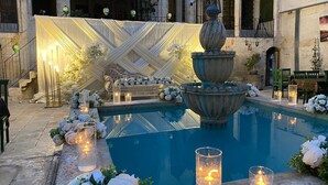 A pool area with a fountain, surrounded by white flowers and candles, set in a courtyard with arches and a white draped backdrop. - Hanehan Butik Otel (Sanliurfa)