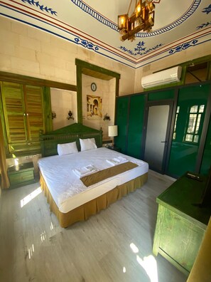 A hotel room with a large bed, green walls, a wooden headboard, a green dresser, a painting on the wall, and an air conditioning unit. - Hanehan Butik Otel (Sanliurfa)
