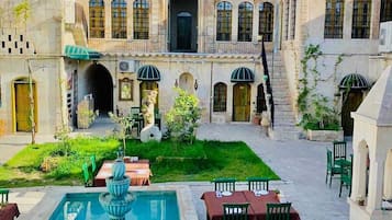 A courtyard with a pool, outdoor seating, and a building with arched windows and a tiled roof.