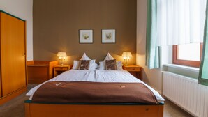 Una habitación de hotel con una cama grande, dos mesitas de noche con lámparas, una ventana con cortinas y dos cuadros en la pared.