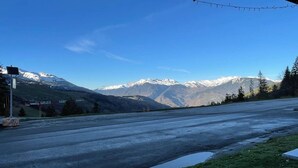 A road with snow-capped mountains in the background, a clear sky, and a grassy area with a building on the left. - Divisible studio for 4 in Valmorel near slopes, shops and lifts (Valmorel)