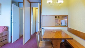 A compact room with a wooden dining table, benches, and a small kitchen area visible through an open door. - Divisible studio for 4 in Valmorel near slopes, shops and lifts (Valmorel)