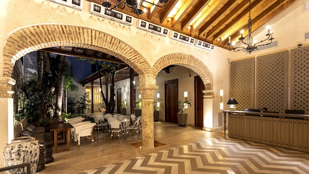 Un vestíbulo con suelo de espiga, columnas de ladrillo en arco, un mostrador de recepción y una zona de estar con mesas y sillas.
