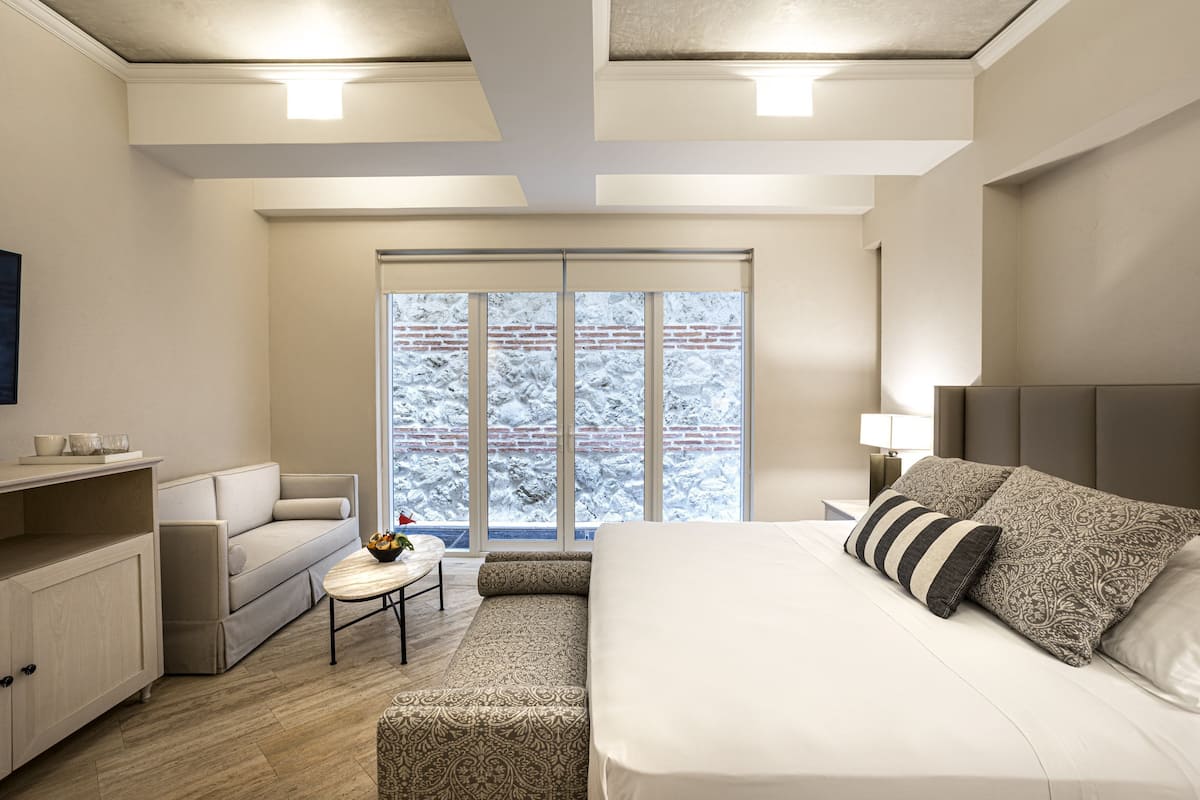 Une chambre d’hôtel moderne avec un grand lit, un canapé, une petite table et une vue sur un paysage enneigé par la fenêtre.