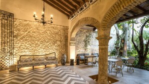 Un interior acogedor con una pared de piedra, un sofá, una araña y un comedor con sillas y mesas.