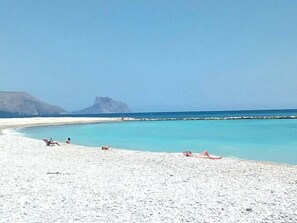 Ein Strand mit weißem Sand, klarem türkisblauem Wasser und einem Felsen im Hintergrund.