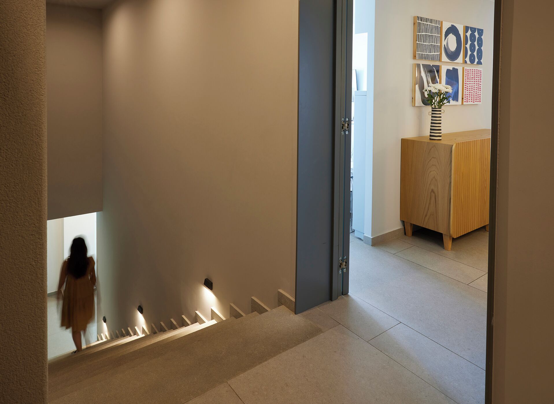 Un interior moderno con una escalera que lleva a una habitación con un armario de madera y decoración mural.