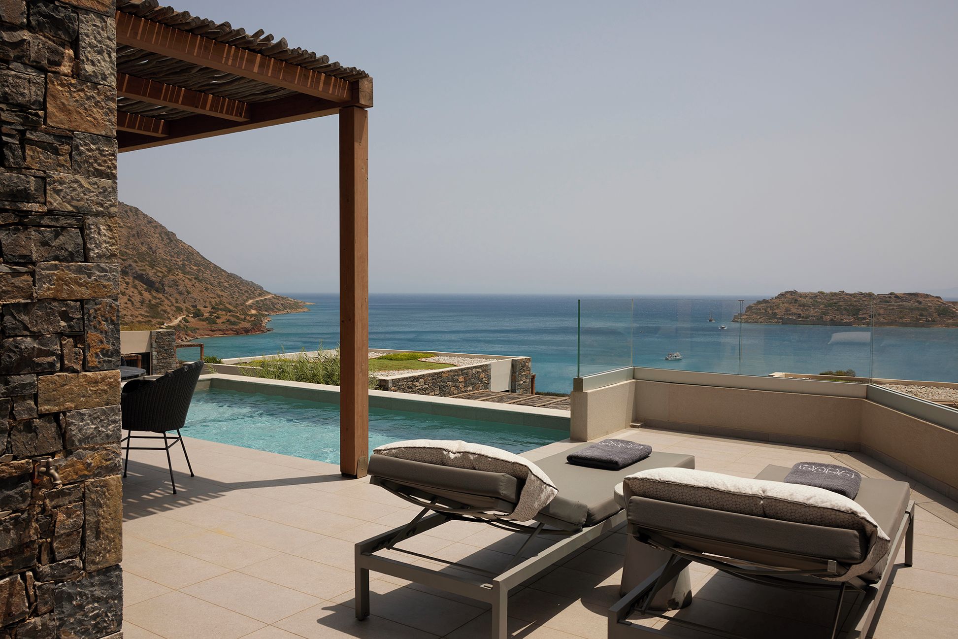 A poolside area with lounge chairs and a pergola overlooking a coastal view.