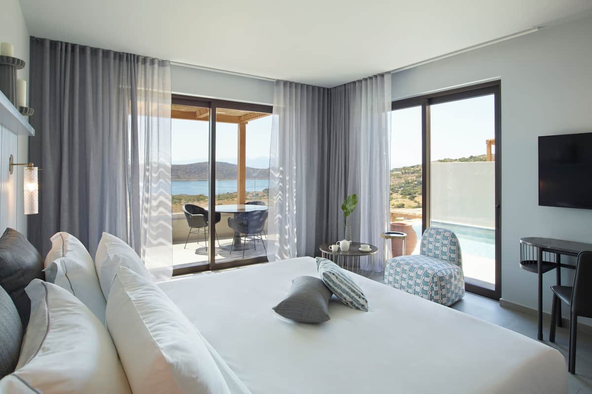 A modern hotel room with a large bed, a balcony with a table and chairs, and a view of the sea.