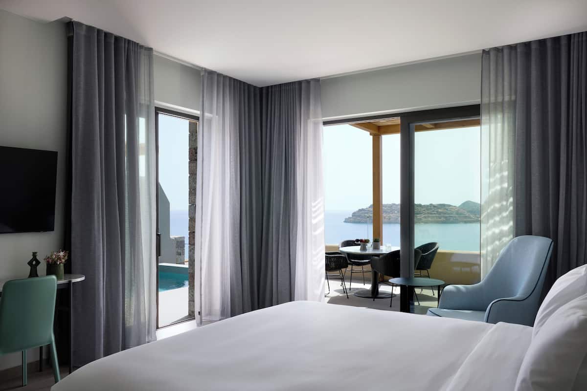 A hotel room with a large bed, a desk, and a view of the sea.