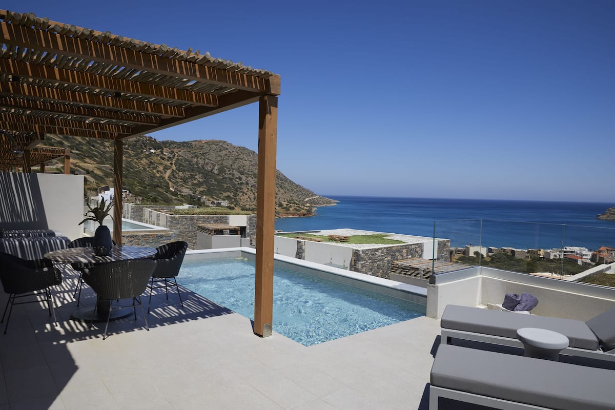 A rooftop pool area with a pergola, lounge chairs, and a view of the sea.