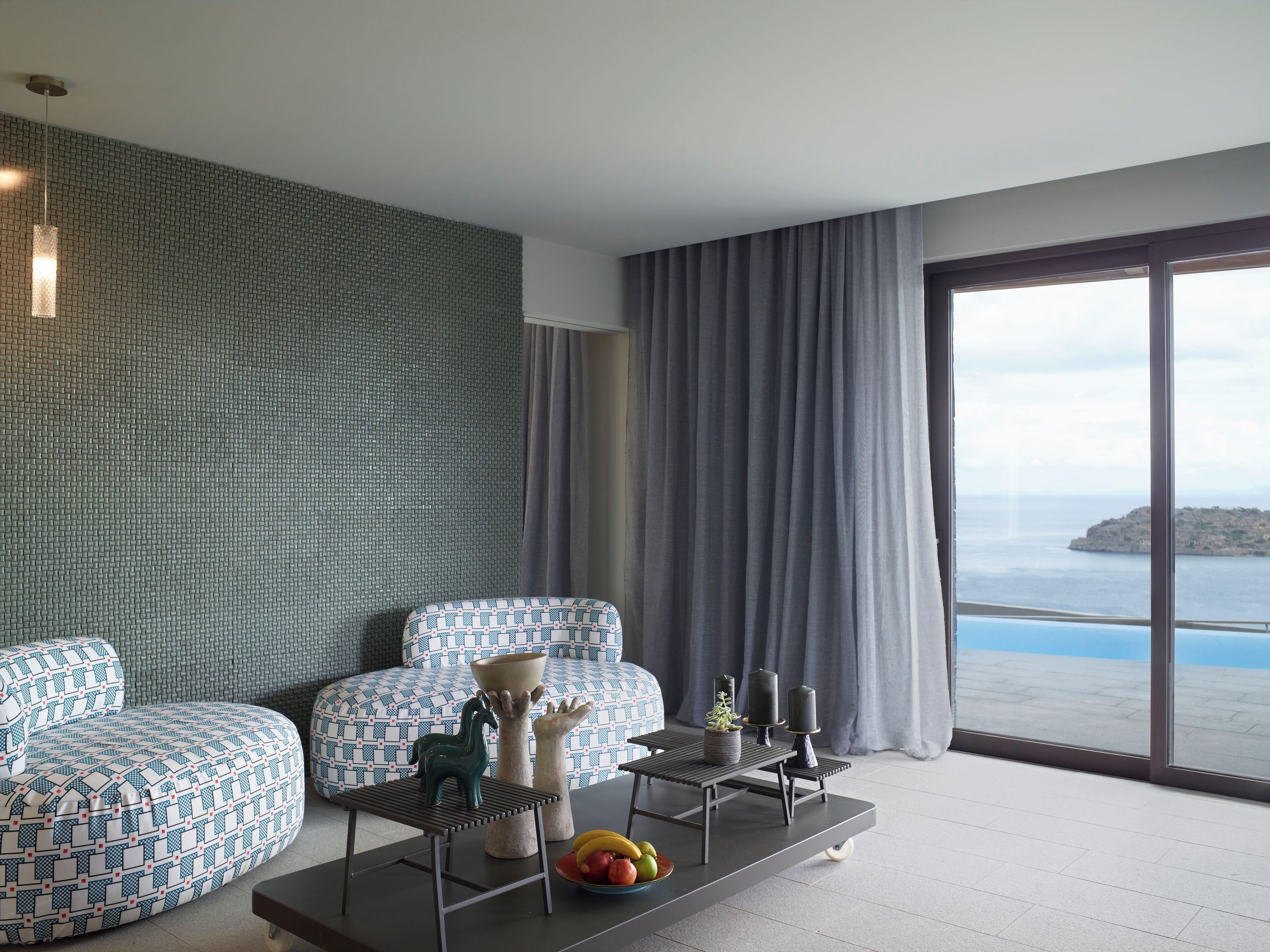 Una sala de estar moderna con un sofá estampado, una mesa de centro con objetos decorativos y vistas al mar a través de amplios ventanales.